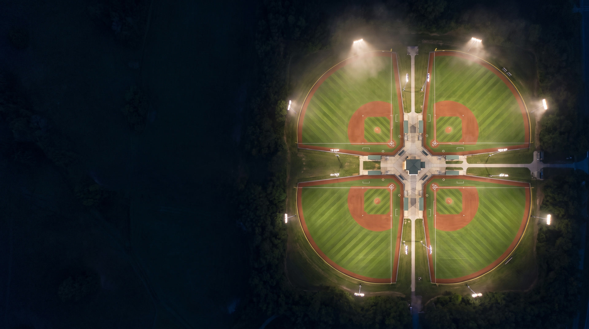 Four lit youth baseball fields at night, seen from above